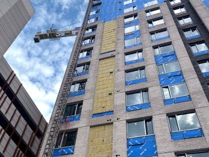 The Metro, wide view of the high-rise facade with GreenGirt Steel and mineral wool insulation exposed in a vertical strip between sections of brick veneer, tower crane alongside