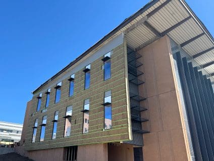 NREL EMAPS building, three-story wall with mineral wool insulation held by GreenGirt Max CMH smooth girts showing as green lines, tall windows with sunshade brackets, and a deep roof overhang above tan panel cladding